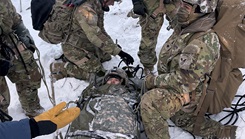 Medical personnel practice securing a patient into a specialized litter during cold weather training in Alaska.