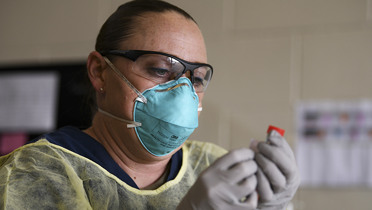 Image of Medical personnel wearing a mask, looking at a vial.