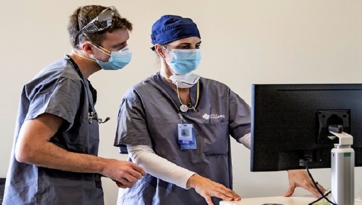 Image of Two hospital personnel, wearing masks, looking at a computer screen.