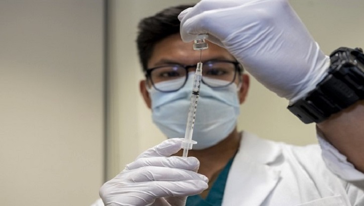 Image of Medical personnel filling a syringe from a vaccine bottle.