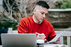 Man wearing sweater sits outside with paperwork