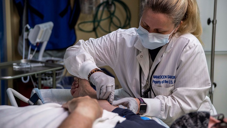 Image of Medical personnel, wearing a mask, inserting an IV into a patient.