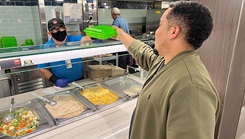 Fernando Rodriguez, food service worker, hands a reusable food container to Corey Toye, Public Affairs multimedia specialist, at Brooke Army Medical Center, Fort Sam Houston, Texas, May 22, 2023. In an effort to reduce waste, BAMC dining encourages the use of reusable take out containers. (DOD photo: Jason W. Edwards)