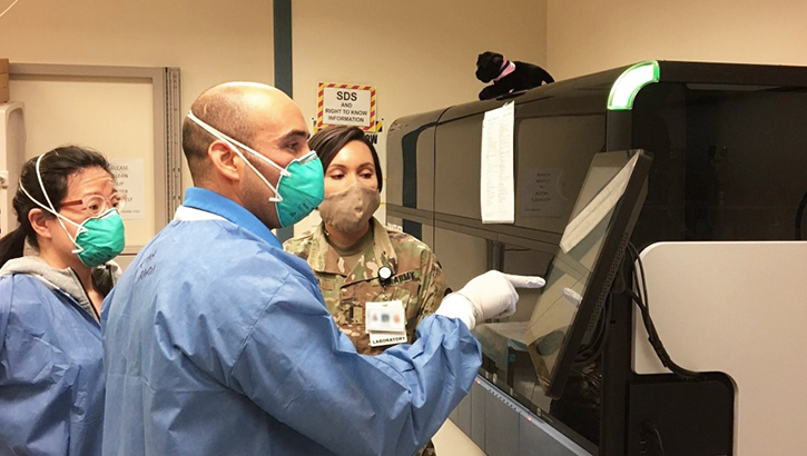 Image of Three lab technicians in full PPE looking at computer screen.