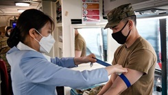 Military personnel wearing a face mask drawing blood during a blood drive