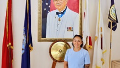 Jessica Hernandez, Physical Evaluation Board Liaison (PEBLO) at Navy Medicine Readiness and Training Command (NMRTC) Twentynine Palms, stands in front of a portrait of Medal of Honor recipient Robert E. Bush, the namesake of the hospital where she supports active-duty service members daily