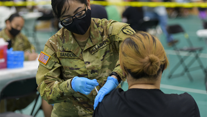 Image of Military health personnel wearing a face mask administering the COVID-19 vaccine.