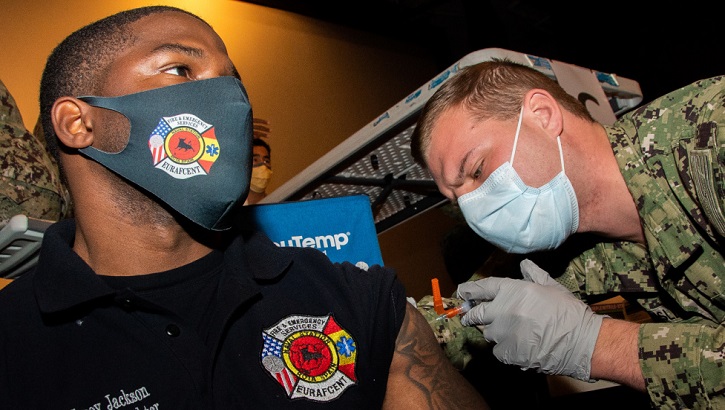 Image of Two soldiers, wearing masks: one is getting a vaccine in his left arm.