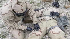 A soldier wearing mission oriented protective posture gear prepares to test the Advanced Anticonvulsant System, Rafa Midazolam Auto-Injector on a fellow soldier at Camp Bullis, Texas. (Photo by Tristan English, Joint Base San Antonio)