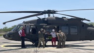 A group of Red Cross and military members prepare to load a person on to a helicopter. 