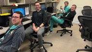 Four smiling fellows working at their desks.  