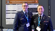 Residents pose in front of a poster at a National Conference. 