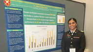 A smiling resident in front of a research poster at a conference. 