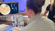 An Ob-Gyn resident looks at a larger screen while maneuvering simulated equipment.  