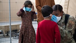 An Airman adjusts the face mask on an Afghan child.