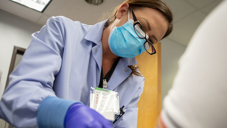 Image of Military health personnel wearing a mask giving a shot to a patient.