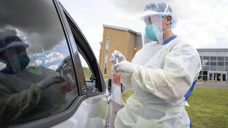 Image of Military personnel in full PPE at a car window demonstrating a swabbing technique.