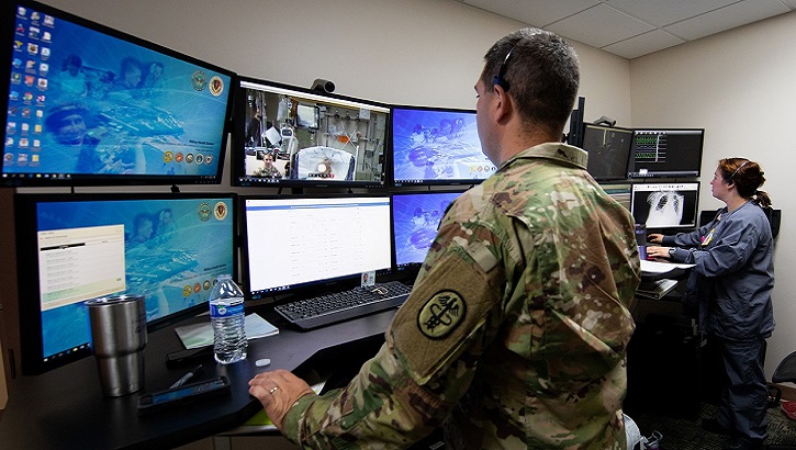 Image of Uniformed service member stands behind wall of computer screens .