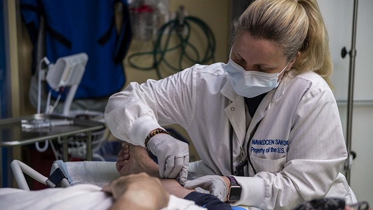 Image of Military health personnel sticking an IV in a patient's arm.