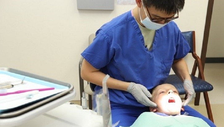 Image of Military health personnel wearing a face mask examines the mouth of a child.